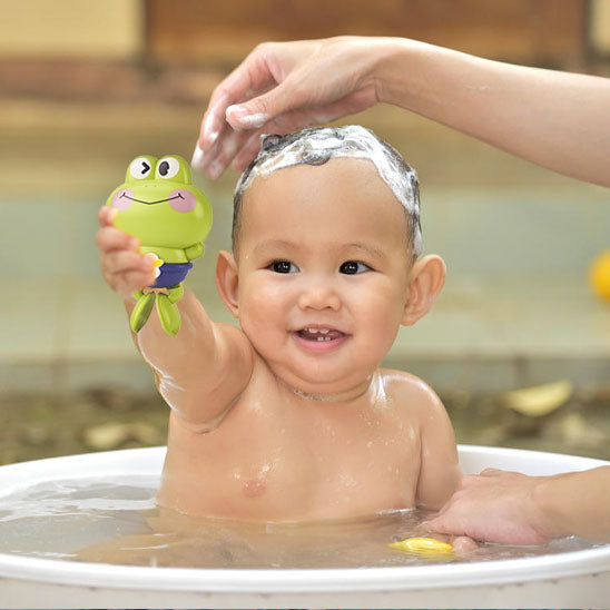 Bébé lève son jouet de bain grenouille pendant que sa maman applique du shampoing moussant