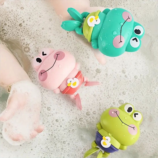 Trois jouets de bain grenouilles vertes, bleu et roses flottent dans une eau mousseuse