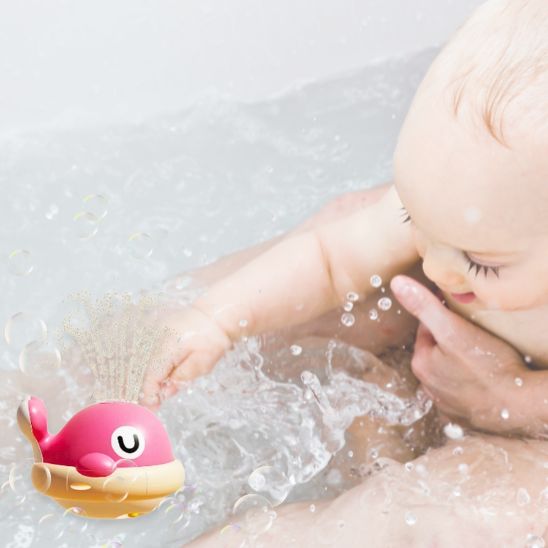 Bébé très content dans sa baignoire et occupé avec son jouet de bain baleine rose qui fait des jets d'eau
