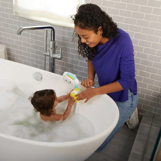 Scène de bain familiale avec une maman souriante qui encourage son enfant à appuyer sur le bouton du jouet de bain nuage éducatif reproduisant le cycle de l’eau.