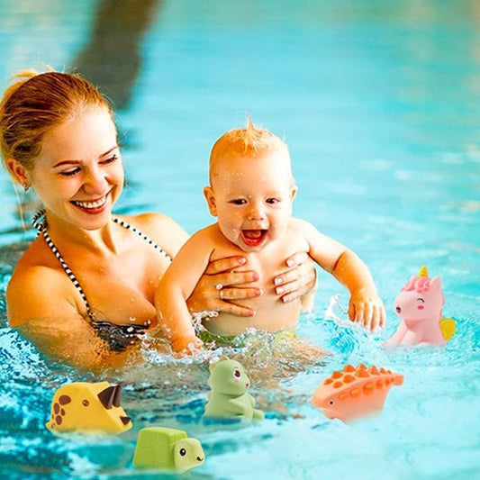 Maman qui porte son bébé émerveillé en jouant avec des jouets de bain animaux safari flottants dans la piscine