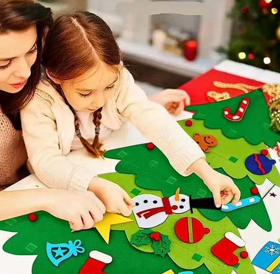 Fillette concentrée pour accroches les ornements sur son sapin de noël en feutre avec la participation de sa maman